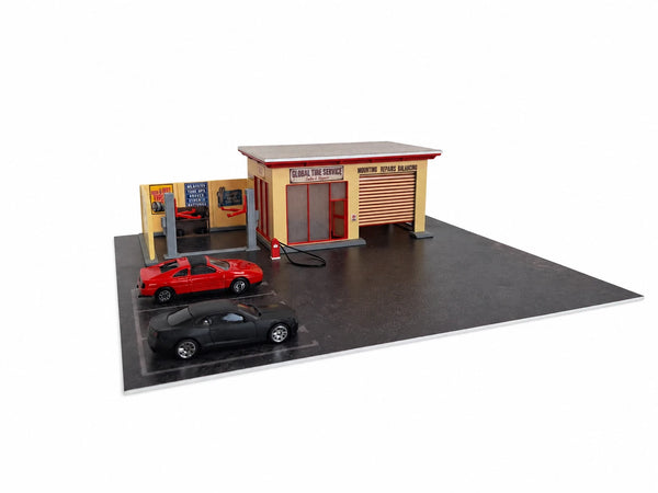 A miniature model of a tire service garage and auto repair shop set on a black baseplate with two toy cars, photographed on a white background.