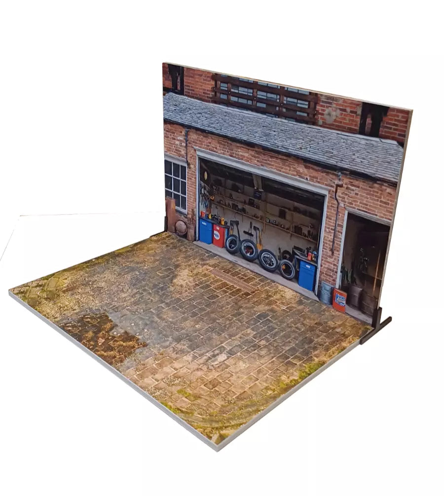 A diorama model kit depicting a vintage garage with a brick wall, cobblestone ground, and various car tires and equipment arranged inside.