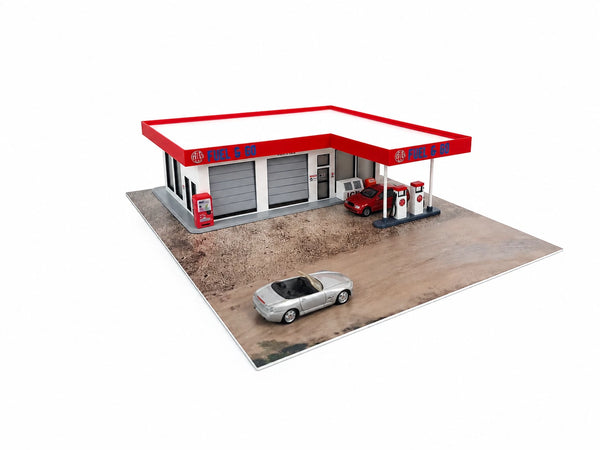 A miniature model of a gas station with a red and white canopy, gray garage doors, red fuel pumps, a small red car, and a silver convertible car on a printed ground surface, isolated on a white background.