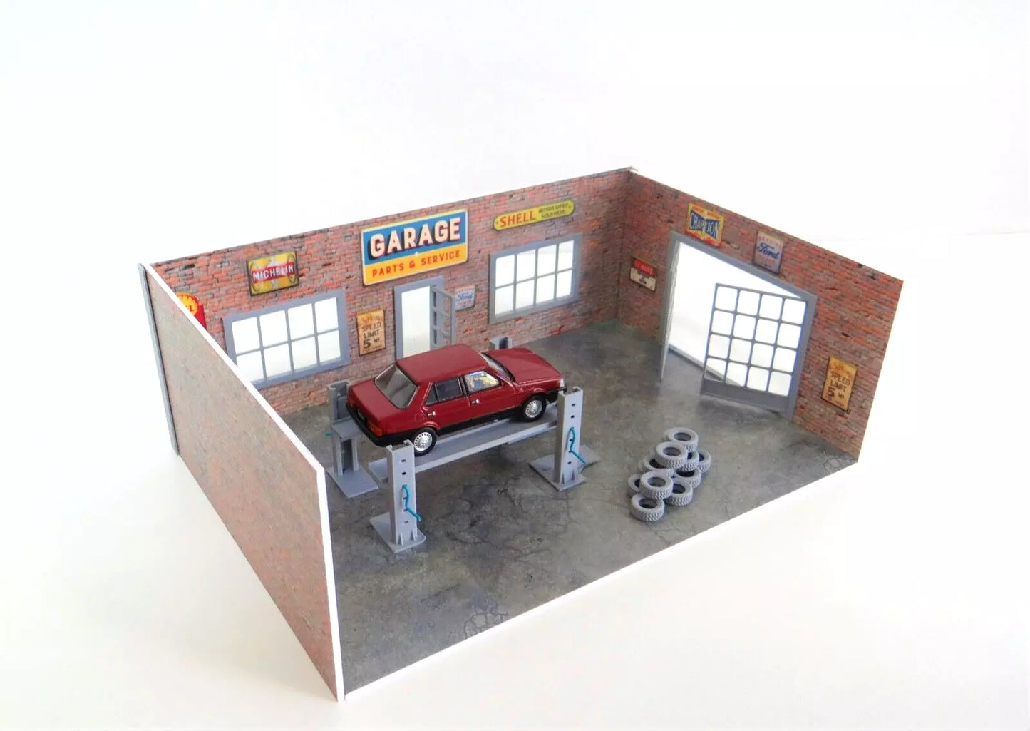 Model garage with a red car on a lift and tires on a stand.