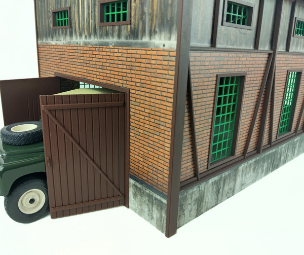 Model of a brick building with a brown door and green windows on a white background