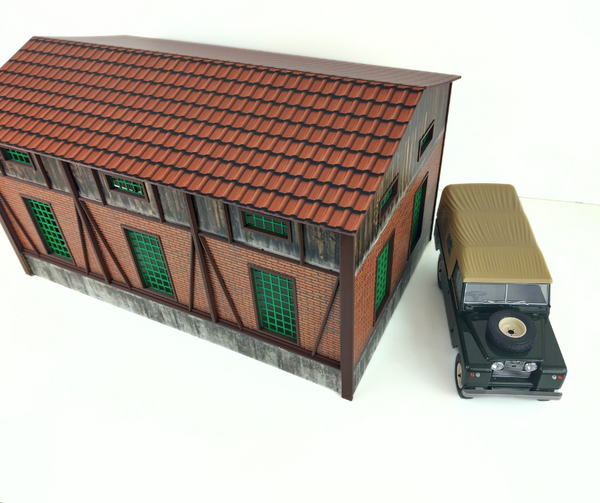 Model of a building with a red roof and a toy car next to it on a white background