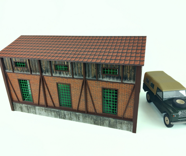 Model of a building with a tiled roof and a toy car next to it on a white background
