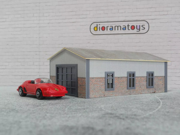 Model garage with a red car in front of a gray brick wall featuring 'dioramatoys' branding.