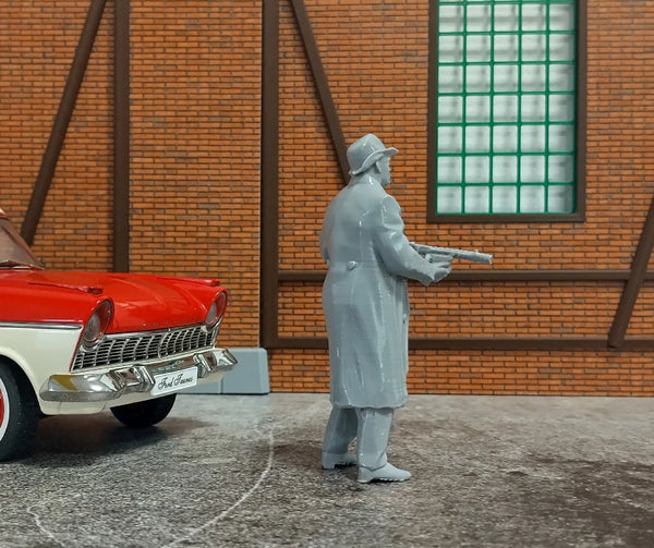 Model figure of a person in a trench coat next to a red car in front of a brick wall.