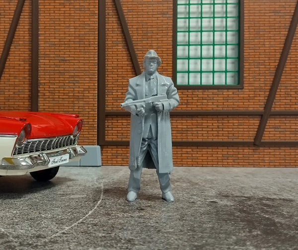 Model figure of a man in a coat standing next to a red car in front of a brick wall.