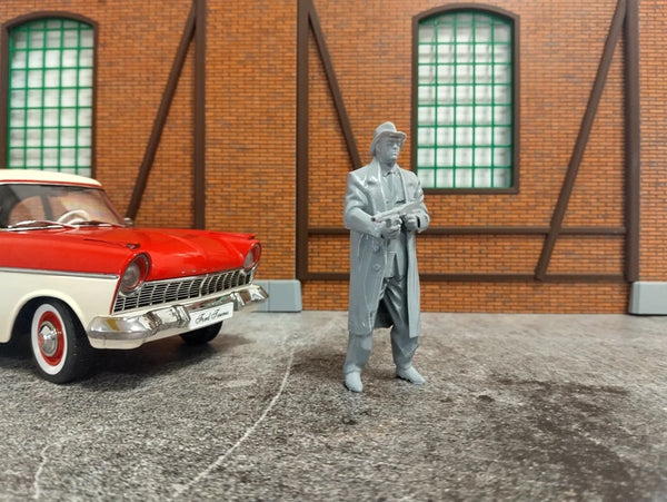 Model figure of a man in a suit standing next to a red vintage car in front of a brick wall.