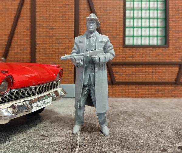 Model figure of a man in a suit holding a gun next to a red car in front of a brick wall.