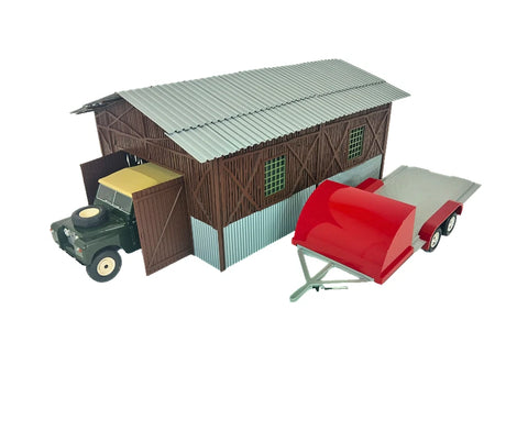 Model of a barn with a roof and a red trailer in front on a white background