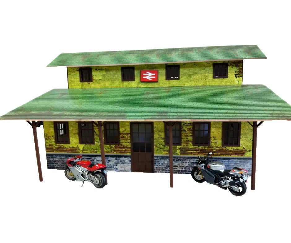 Model train station with green roof and brick wall, featuring two motorcycles in front.
