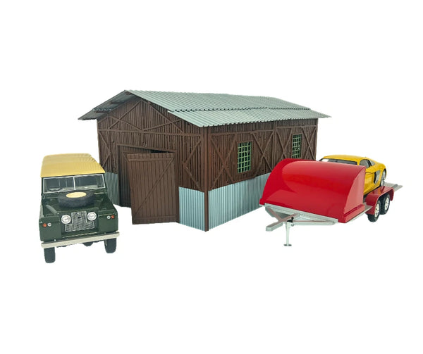 Model barn with toy cars and a red trailer on a white background